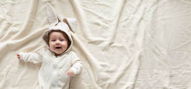 Cute little baby in bunny costume on blanket at home top view