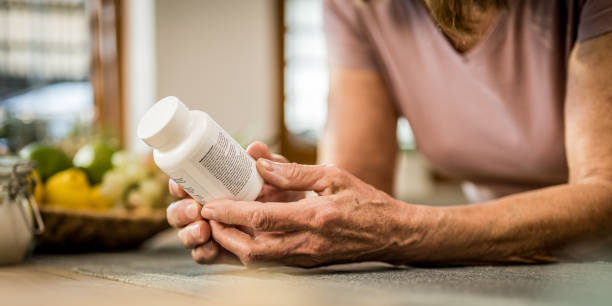 Close-up of senior woman holding pill bottle in domestic kitchen