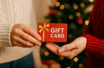 A person handing a red gift card with a gold ribbon to another person in front of a softly lit Christmas tree.